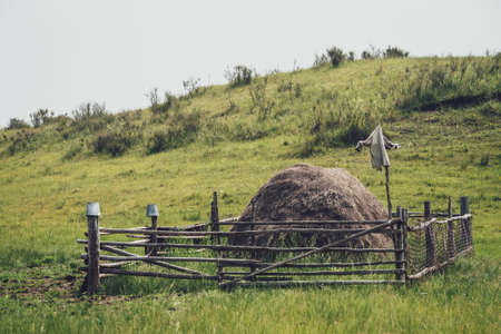 Beautiful foggy mountain landscape with scarecrow on wooden fence around haystack in mountains in vintage tones. Stack of hay is surrounded by wood fence with scarecrow on background of hills in fog.の写真素材
