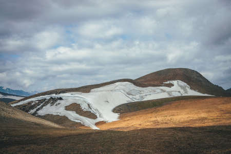 Sunny mountain desert relief with glacier in sunlight under low cloudy sky. Scenic highlands landscape with small glacier high in mountains on hills. Minimalist mountain scenery of highland desert.の写真素材