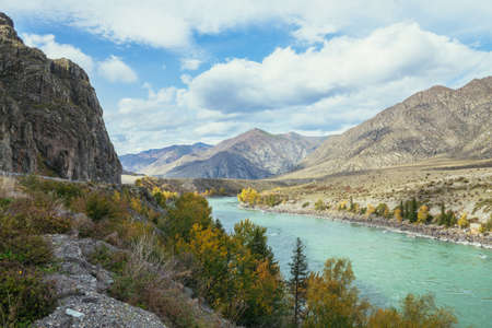 Colorful autumn landscape with golden leaves on trees along wide turquoise mountain river in sunshine. Bright alpine scenery with big mountain river and yellow trees in gold autumn colors in fall timeの写真素材