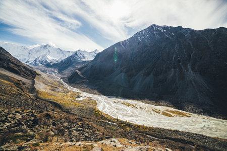 Beautiful alpine landscape with great sharp rocky peak and mountain river with many streams in valley in autumn color in sunshine. Awesome sunny scenery with high mountain wall with snow in sunlight.の写真素材