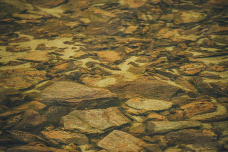 Beautiful fragment of orange stony bottom of mountain lake with transparent water. Colorful minimal nature background with many orange stones with mosses and lichens on bottom of mountain lake.の写真素材