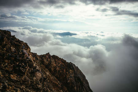 Sharp rocks on background of mountain peak above cloudy sky. Mountain vertex floats in thick clouds. Minimalist landscape with mountain top above dense low clouds. Scenic minimalism over dense clouds.の写真素材