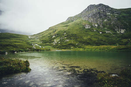 Atmospheric mountain landscape with rainy circles on clear lake water. Sandy bottom of mountain lake with stones. Beautiful scenery with circles of rain on transparent water surface in rainy weather.の写真素材