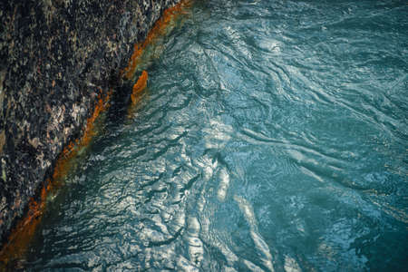 Nature background with rocky shore of deep green lake. Texture of dark blue calm water of lake. Meditative ripples on water surface. Edge of clear dark turquoise water. Full frame of lake fragment.の写真素材