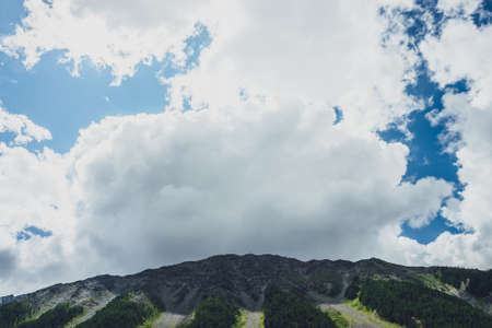 Awesome scenery with shadow of big cloud on high mountain top. Huge white cloud in blue sky over...
