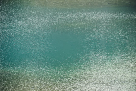 Texture of green blue calm water of lake. Meditative ripples on water surface. Nature minimal background of green blue lake with golden shine. Natural backdrop of lake fragment with clear azure water.の写真素材