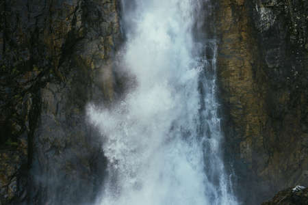 Atmospheric minimal landscape with vertical big waterfall on rock mountain wall. Powerful large waterfall in dark gorge. Nature background of high vertical turbulent falling water stream on wet rocks.の写真素材