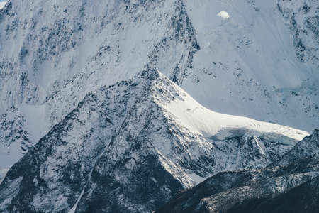 Awesome mountain landscape with big snow rock with peaked top on background of giant snow-covered mountain wall in sunshine. Atmospheric scenery with snowy mountains in sunlight. Great snowy mountainsの写真素材