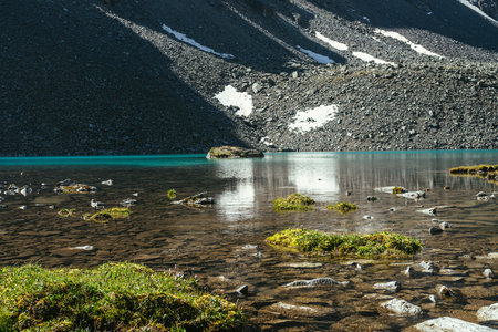Beautiful scenic landscape with turquoise mountain lake with transparent water and stony bottom. Azure glacial lake with clear water surface in sunlight. White snow and green grass near mountain lake.の写真素材