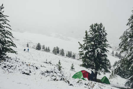 Scenic winter landscape with green tent and red tent on snowy hill with coniferous trees on...