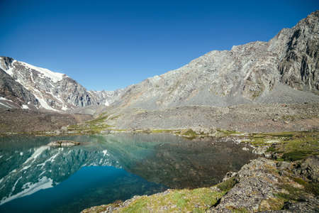 Snowy mountain reflected in clear water of glacial lake. Beautiful sunny landscape with glacier reflection in water surface of mountain lake under clear sky. Snow on rock reflected in mountain lake.の写真素材