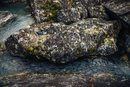 Scenic nature background of turquoise clear water stream among rocks with mosses and lichens....