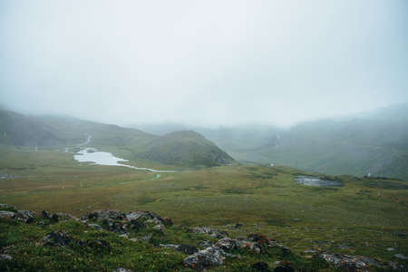 Atmospheric alpine view to beautiful mountain lake among hills during rain. Scenic landscape with snowfall in high mountains. Low clouds in highlands in rainy weather. Overcast mountain landscape.の写真素材