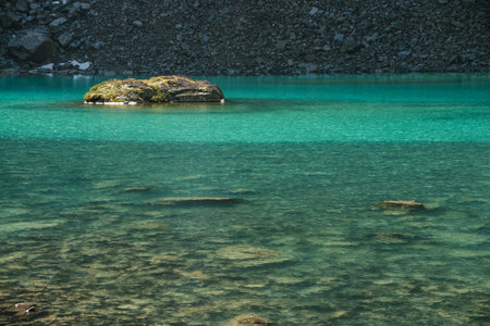 Beautiful landscape with mossy rock in turquoise mountain lake with transparent water and stony bottom. Azure glacial lake in sunlight. Colorful scenery with mossy stone above clear water surface.の写真素材