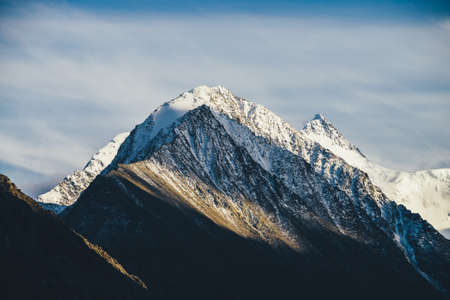 Atmospheric alpine landscape with two rocky pointy mountain peaks with snow in golden sunshine under...