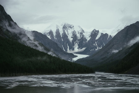 Atmospheric alpine landscape with mountain streams from snowy mountains in overcast weather. Bleak monochrome scenery with glacier tongue in mountain valley in rainy weather. Glacier among low clouds.の写真素材