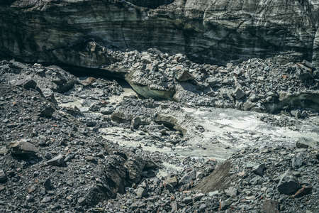 Scenic landscape with mountain river beginning from glacier among large moraines. Beautiful scenery...