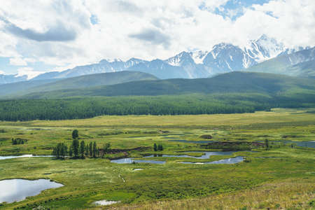 Beautiful green scenery with lake system on tableland among forest hills and snowy mountains. Scenic landscape with lakes group on plateau. Blue lakes system in wide valley. System of mountain lakes.の写真素材