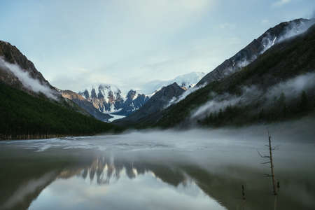Atmospheric alpine landscape with snowy mountains in golden sunlight reflected on mirror mountain...