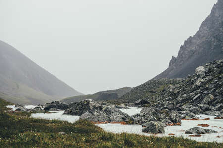 Atmospheric landscape with mountain creek among moraines in rainy weather. Bleak scenery with milky river among rocks. Gloomy view to mountain river. Stones with moss and lichen in milk water stream.の写真素材