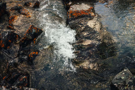 Scenic nature background of clear water stream among rocks with orange lichens. Atmospheric mountain landscape with lichen stones in transparent water of mountain creek. beautiful mountain stream.の写真素材