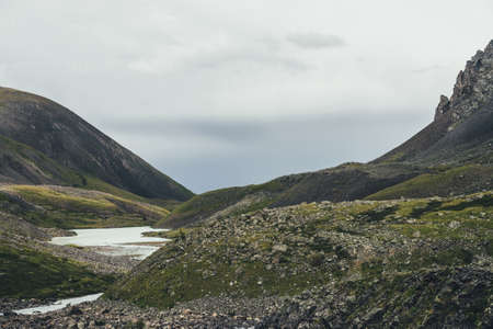 Atmospheric mountain landscape with mountain lake near sharp rocks in narrow valley in rainy weather. Bleak overcast scenery with mountain lake among rocky hills in highland glen under gray cloudy skyの写真素材
