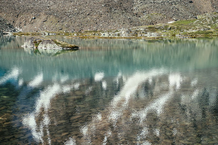 Rock in turquoise mountain lake. Snowy mountain reflected in azure clear water of glacial lake. Beautiful sunny background with snow-white glacier reflection in green water surface of mountain lake.の写真素材