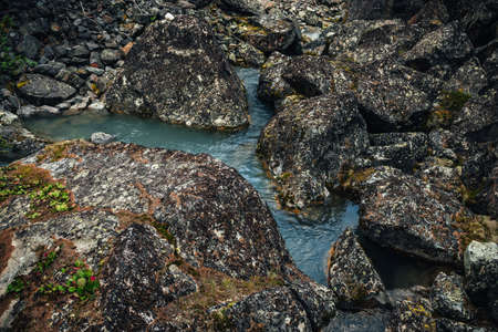 Scenic nature background of turquoise clear water stream among rocks with mosses and lichens....