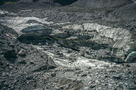 Scenic landscape with mountain river beginning from glacier among large moraines. Beautiful scenery with glacier at source of river. Mountain creek from ice among big stones. River source from glacierの写真素材