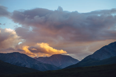 Beautiful mountain scenery with golden dawn light in cloudy sky. Scenic mountain landscape with illuminating color in sunset sky. Silhouettes of mountains on sunrise. Gold illuminating sunlight in skyの写真素材