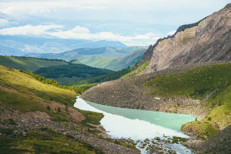 Colorful green landscape with beautiful turquoise mountain lake in sunlight. Impressive scenery with turquoise lake on background of green mountains with forest and low clouds. Scenic mountains view.の写真素材
