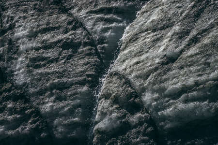 Minimalist nature background with water stream on glacier surface with cracks and scratches. Minimal natural backdrop of icy wall with stream. Shiny glacial surface. Beautiful texture of glacial wall.の写真素材