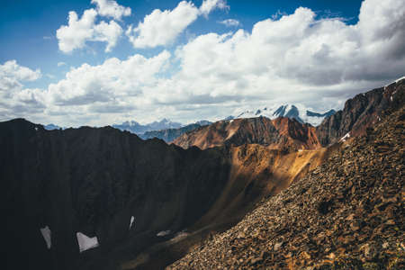 Scenic highlands landscape with great snowy mountain peak behind colorful brown red orange mountain wall in sunlight. Sunny mountains scenery with high vivid brown red orange mountain and big snow topの写真素材