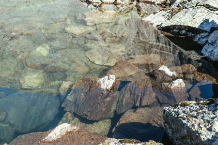 Beautiful nature background of stony bottom in transparent water of glacial lake in sunlight. Sunny nature backdrop with many stones in clear water of glacier lake. Invisible water of mountain lake.の写真素材
