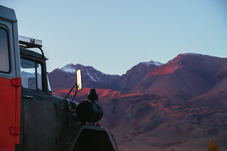 Minimal closeup of orange truck with view to pink magenta purple mountains with snow and sharp rocks on top in blur under blue clear sky in sunset sunlight. Russia, Altai Republic, 20 September, 2020.のeditorial素材