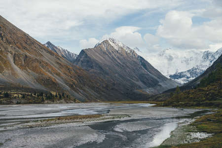 Scenic autumn landscape with many water streams in valley with view to big rock with snow on top and beautiful high snowy mountains in sunshine. Mountain creek and great snow-covered mountain wall.の写真素材