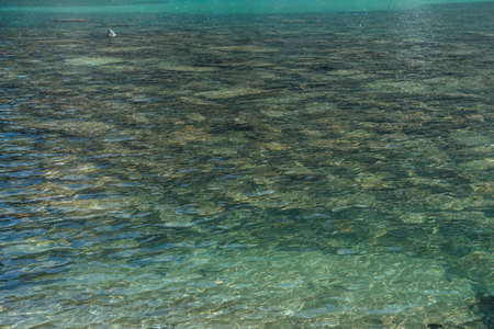 Meditative ripple of mountain lake. Beautiful relaxing background of stony bottom in turquoise transparent water of glacial lake in sunlight. Sunny backdrop with many stones in green clear water.の写真素材