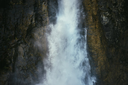 Atmospheric minimal landscape with vertical big waterfall on rock mountain wall. Powerful large waterfall in dark gorge. Nature background of high vertical turbulent falling water stream on wet rocks.の写真素材