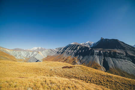 Awesome autumn landscape with great snow-covered mountains and sharp rockies. Spectacular colorful view to mountain ridge and yellow valley in fall. Wonderful mountain scenery in orange autumn colors.の写真素材