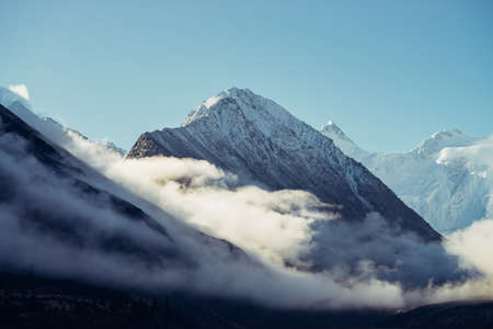 Beautiful view of snow-capped mountains above thick clouds in sunshine. Scenic bright mountain landscape with white-snow peak among dense low clouds in blue sky. Wonderful scenery with snowy pinnacle.の写真素材