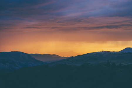 Atmospheric landscape with silhouettes of mountains with trees on background of vivid orange blue violet dawn sky. Colorful nature scenery with sunset or sunrise of illuminating color. Sundown paysageの写真素材