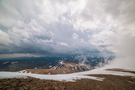 Awesome top view through clouds to high snowy mountains. Scenic landscape with beautiful snow mountains in low clouds. Atmospheric alpine view from stone hill to snow mountain range with low clouds.の写真素材