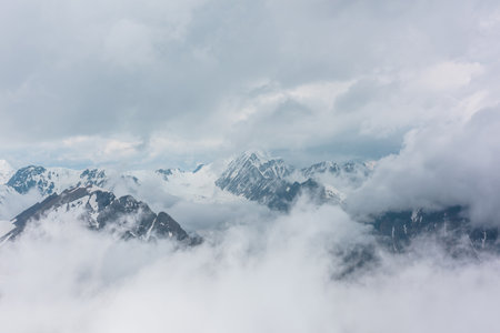 Awesome aerial view to high snowy mountains in dense low clouds. Minimal landscape with beautiful mountain peaks in thick clouds. Simple minimalism with snow mountain tops in cloudy sky above clouds.の写真素材
