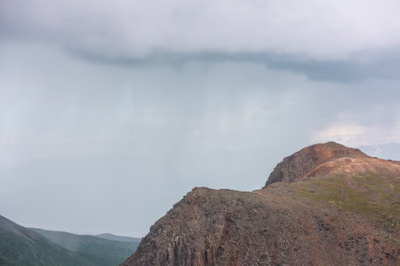 Dramatic aerial landscape with sunlit mountain top during rain at changeable weather. Atmospheric mountain scenery with sharp rocks in sunlight under lead gray cloudy sky. Rainy clouds in mountains.の写真素材