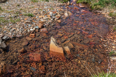 Sharp stone in clear water stream with motley stony bottom in sunlight. Colorful mountain stream...