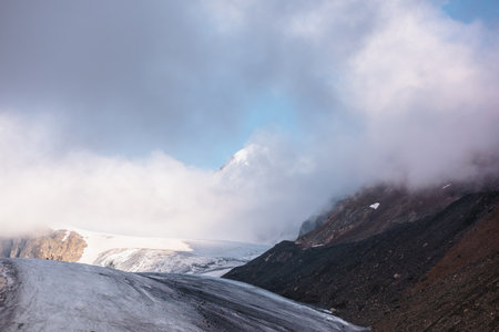 Scenic mountain landscape with large glacier in low clouds in sunrise colors. Colorful view to...