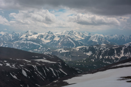 Awesome aerial view to high snow mountains under cloudy sky. Gloomy mountain landscape at very high altitude with cloudiness. Dark atmospheric mountain scenery with snowy mountain range in overcast.の写真素材
