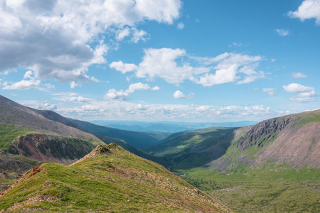 Scenic view from mountain ridge to green forest valley among mountain ranges and hills on horizon at changeable weather. Green landscape with sunlit mountain vastness under cumulus clouds in blue sky.の写真素材