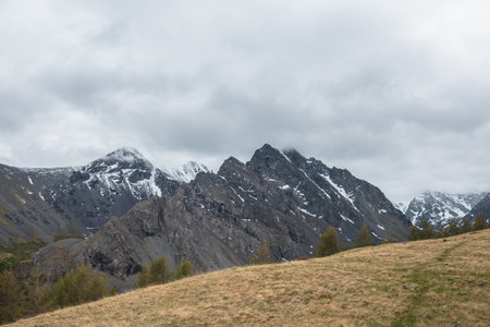 Atmospheric landscape with large thorny dragon shaped mountain top under gray cloudy sky. Gloomy top view from hill to high snowy mountain range with sharp rocks in shape of dragon back in low clouds.の写真素材