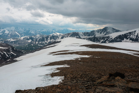 Awesome view from stone hill with snow to high snowy mountain range in overcast. Gloomy alpine landscape at very high altitude with cloudiness. Atmospheric scenery with snow mountains under cloudy skyの写真素材